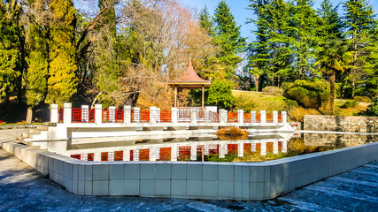 Wooden gazebo and pond framed by white stone in the arboretum of Sochi. Russia