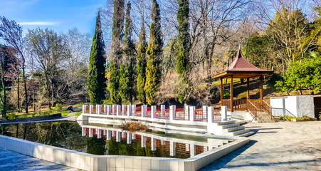 Wooden gazebo and pond framed by white stone in the arboretum of Sochi. Russia