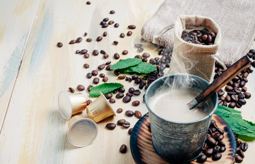 Cup of hot coffee on vintage wooden table with scattered coffee beans and coffee capsules. Copyspace