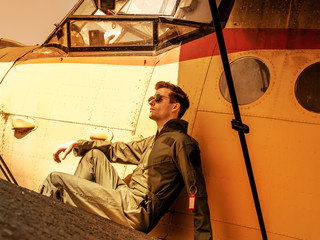A handsome young pilot sitting on the wing of a plane