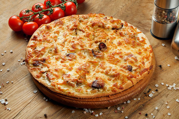 Pizza with melted cheese and tomato on a wooden tray. Pizza in composition with ingredients on a wooden table. Top view.