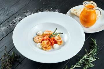 Appetizing, Spanish tomato soup with shrimp and mozzarella in a white plate on a black wooden background. Restaurant serving. Close up