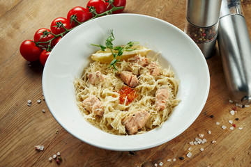Italian homemade tagliatelle with salmon and parmesan in a beige bowl on a wooden background. Tasty pasta. Copy space
