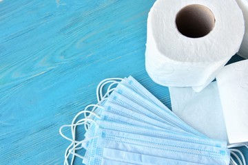 roll of toilet paper and sterile protective masks with selective focus on blue wooden background....