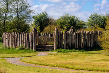 Old wooden palisade of the fort or camp surrounded by green fields and trees. Depicting early age of human settlements