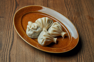 Appetizing homemade khinkali with different fillings (minced meat, cheese, vegetables or spinach) in a brown plate on a wooden background. Traditional Georgian cuisine. Georgian dumplings