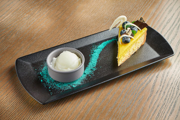 Appetizing cheesecake with blueberries and chocolate, vanilla ice cream on a black plate. Wood background. Close up. Copy space