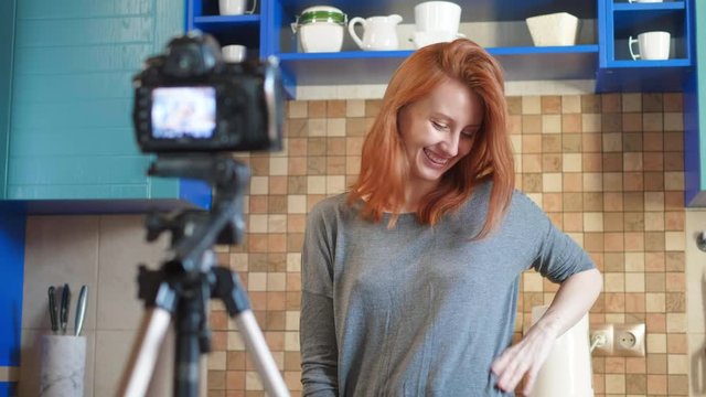 Food blogger girl influencer is recording a video or podcast in the kitchen. Makes lifestyle blog vlog, Shows ok sign from hand. A woman communicates with subscribers, asks to like the video