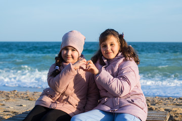 Fototapeta na wymiar two little caucasian girls in jackets happy to be together on the beach