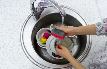 Girl washes dishes at home in the kitchen. Dirty dishes lie in the sink. Washing dishes with a sponge.
