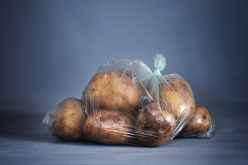 Recycling and environment idea: fresh potato in plastic package, wrapped in plastic cellophane on blue background