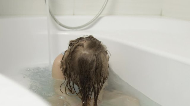 Cute blonde girl takes a bath in swimwear. Little child washes her head