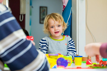 Cute girl playing with many colorful doughs surrounded with unrecognizable family members.