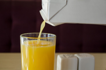 Yellow juice,  orange or mango,  or multifruit,  pours from a white packaging packing juice into a...