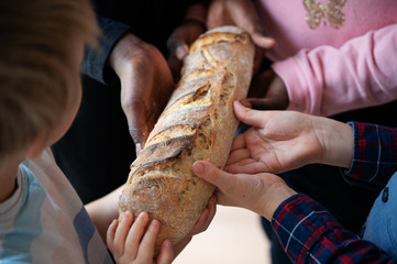 Hands of four children, black and white, holding  one loaf of bread