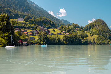 View of Brienz lake with clear turquoise water. Sailing boats. Traditional wooden houses on the...