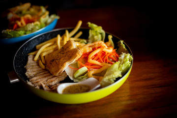 Pork steak with vegetable and grill bread in plate put on wooden table.