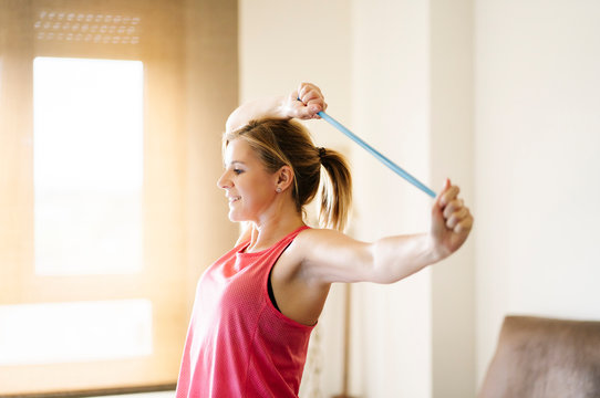 beautiful blonde caucasian athlete woman doing exercises with elastic band in living room at home