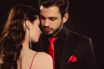 Beautiful woman standing near handsome man in formal wear isolated on black