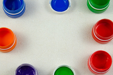 Jars with bright multi-colored gouache, tassels lie on a white background lit by light
