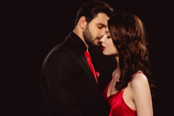 Side view of handsome man kissing elegant girlfriend isolated on black