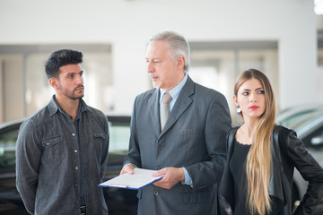 Young family talking to the salesman and choosing their new car in a showroom