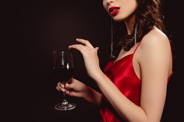 Fototapeta na wymiar Cropped view of elegant young woman holding glass of red wine isolated on black