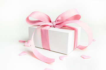White gift box with pink ribbon and a small pink hearts on white background. Selective focus. Copy...