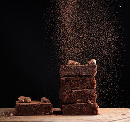 stack of square baked brownie pieces sprinkled with cocoa powder, particles froze in the air...