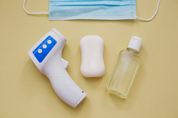 protection during virus outbreak concept: surgical mask, soap, hand sanitizer and infrared thermometer on yellow background