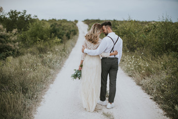 Smiling bride and groom spending time together. Posing on the mountain hills background. Dressed in white dress beautiful blonde caucasian bride and handsome groom. Hugs, kissess and enjoy the company