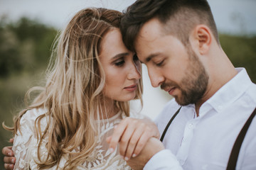 Smiling bride and groom spending time together. Posing on the mountain hills background. Dressed in white dress beautiful blonde caucasian bride and handsome groom. Hugs, kissess and enjoy the company