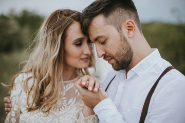 Smiling bride and groom spending time together. Posing on the mountain hills background. Dressed in white dress beautiful blonde caucasian bride and handsome groom. Hugs, kissess and enjoy the company