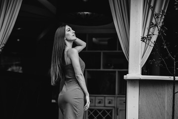 A beautiful young girl is standing on the veranda of a beautiful house. Black and white.