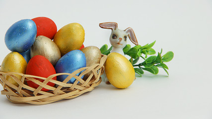 colorful Easter eggs in a wicker basket and an Easter Bunny on a white background