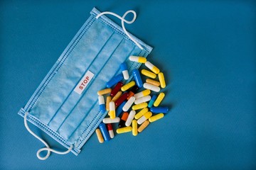 Disposable mask against coronary viral disease 2019 drip infection COVID19. Lies on a blue background with the words Stop and many multi-colored capsules for treatment, antibiotics.