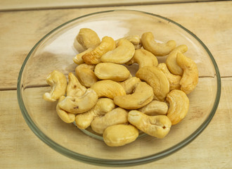 Cashew kernels in a glass plate on a wooden background