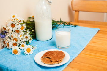 Simply stylish wooden kitchen with bottle of milk and glass on table, summer flowers camomile, healthy foog moring concept