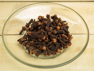 Dry clove spices in glass plate on wooden background