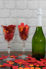 Paper hearts, red tape on the two glasses of champagne, bottle on the stone background.