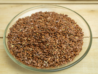 Flax seeds in a glass plate on a wooden background