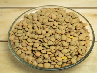 Lentils gray in a glass plate on a wooden background