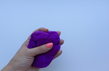 Woman's hand with pink manicure holding a piece of violet wool on white background. Concept of felting creative hobby.