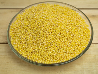 Millet groats on a glass plate on a wooden background
