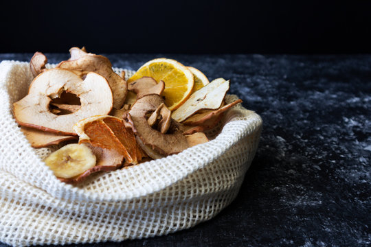 Fruit chips, apple and pear chips on a dark background in a woven string bag
