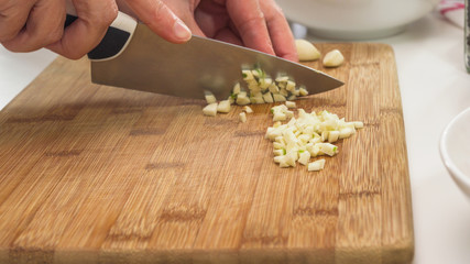 Chopping garlic on a wooden chopping board, close up on a kitchen table, woman hands