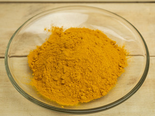 Turmeric powder seasoning in glass plate on wooden background