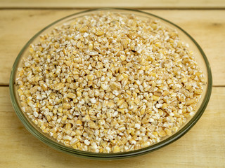 Wheat groats in a glass plate on a wooden background