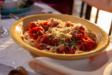 Plate full of pasta, chicken, tomotoes, cheese, ready to eat a delicious meal complete with wine