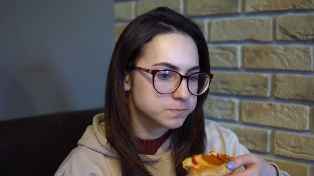 A young woman is eating a slice of pizza. Woman sitting in a restaurant and eating pizza close-up.